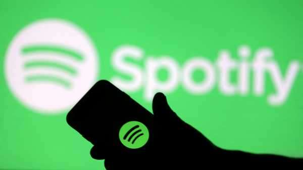 A smartphone is seen in front of a screen projection of the Spotify logo in this picture illustration