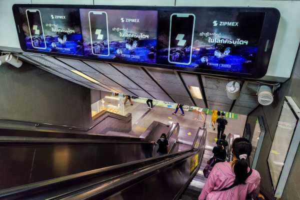 People walk past advertisement screen boards showing a crypto exchange platform 