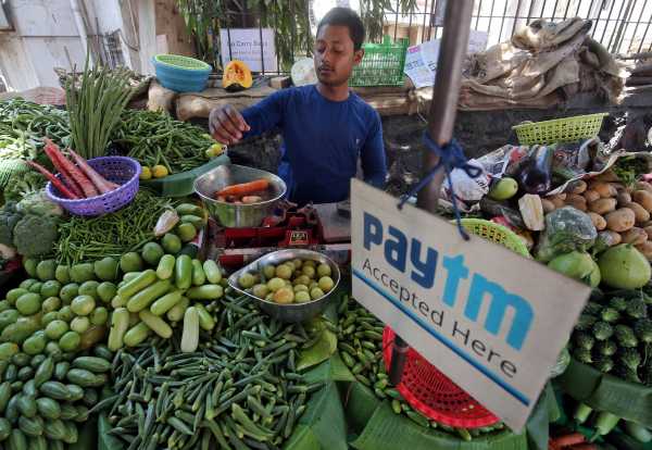 A vendor weighs vegetable next to an advertisement of Paytm, a digital payments firm, hanging amidst his vegetables at a roadside market in Mumbai